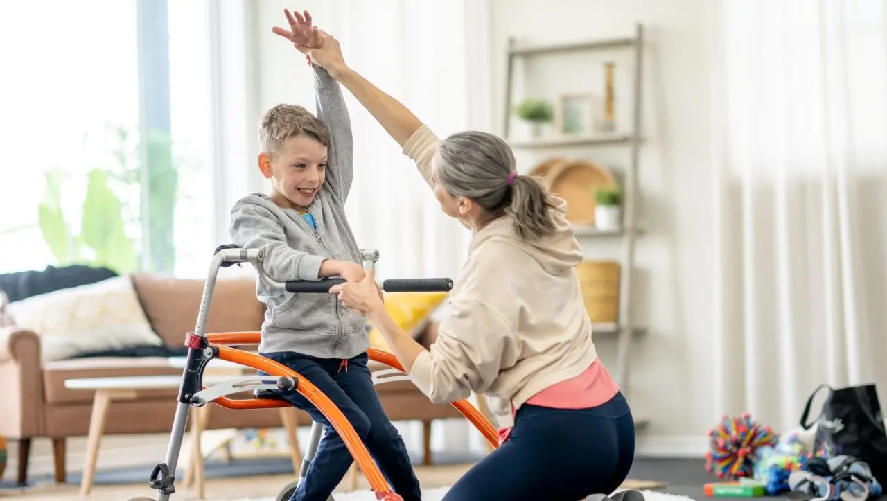 Biokineticist assisting a child with a mobility and rehabilitation exercise using a walker in a therapy session.